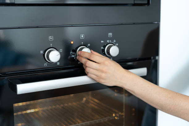 Woman select program turning switch at modern built in oven Cropped view of woman select program turning switch at modern built in oven, select program, standing in kitchen oven stock pictures, royalty-free photos & images