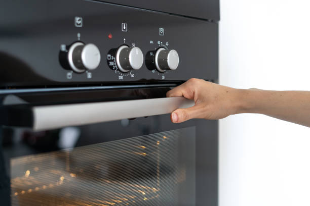 Woman holding handle modern built in oven and opening glass door Cropped view of woman holding hond on modern built in oven handle and opening glass door, standing in kitchen oven door stock pictures, royalty-free photos & images
