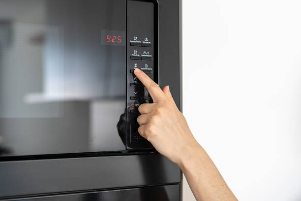 main de fixation de femme sur le bouton noir de micro-ondes - timer cooking domestic kitchen time photos et images de collection