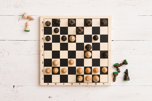 Top view on wooden chess board with figures during the game on white wooden table background
