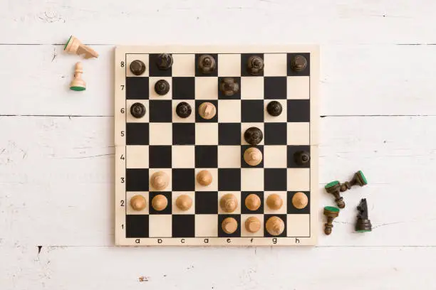 Photo of Top view on wooden chess board with figures during the game on white wooden table background