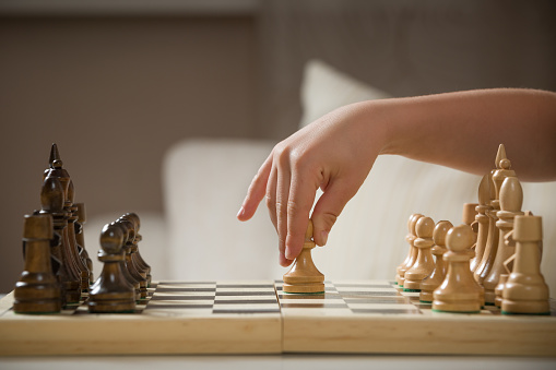 Child's hand holding chess figure while playing chess. Little clever child playing chess at home. Education concept.