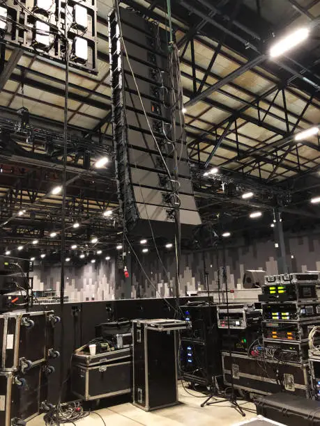 Photo of Installation of professional sound speakers, line array and stage equipment for a concert. Backstage area and tech zone with amplifiers, flight cases and radio microphones.