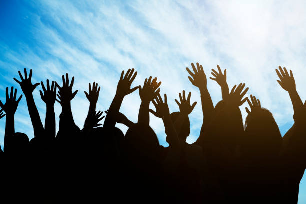 istock Group of people raising their hands against a blue sky 1160644238
