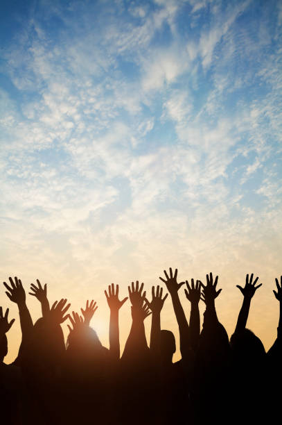 group of people raising their hands against a sunset - hand raised arms raised multi ethnic group human hand imagens e fotografias de stock