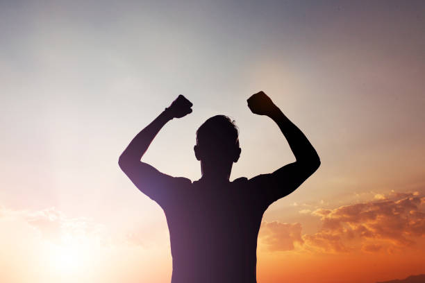 silhouette of man cheering success against sunset with arms raised - cheering men shouting silhouette imagens e fotografias de stock