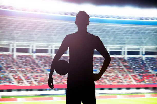 Photo of Silhouette of soccer player standing in stadium with a ball