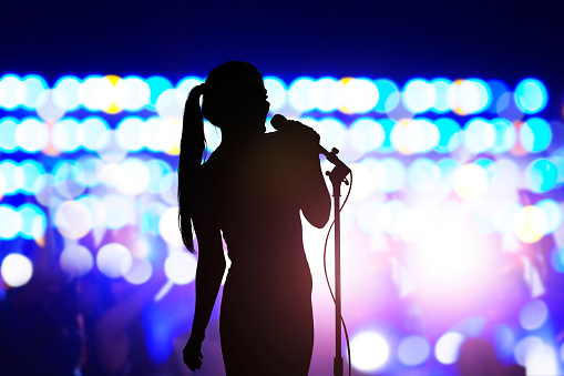 Silueta de mujer con micrófono cantando en el escenario de conciertos frente a la multitud photo