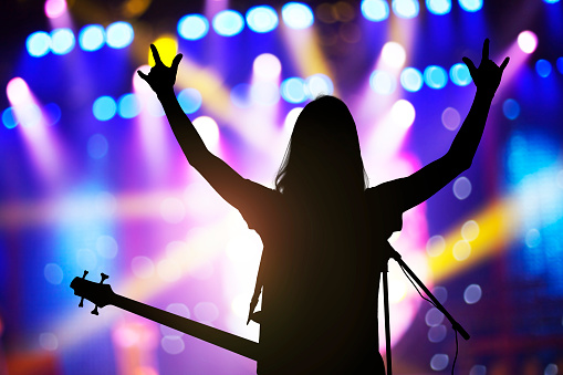 Silhouette of musician with long hair cheering with crowd on concert stage with hands raised