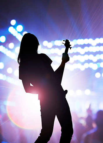 Silhouette of rock musician playing on guitar on concert stage at festival