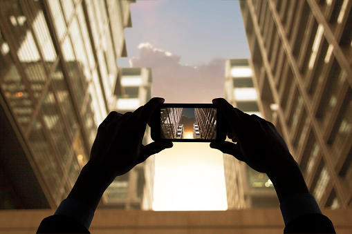 Hands photographing skyscraper buildings at sunset