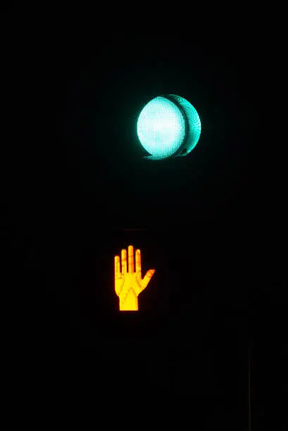 Illuminated stop walk sign with green illuminated car streetlight taken at night with black background