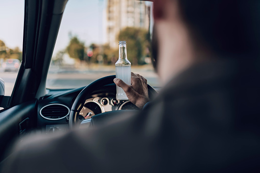 Driver Behind the Wheel of a Car Holds a Bottle of Alcohol in His Hand. Man Drinking Alcohol While Driving a Car. Danger on the Road Caused by Drunken Drivers. Transportation, Alcohol, Vehicle and People Concept