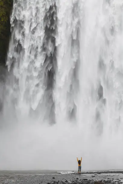 Photo of Happy woman enjoying near Skogafoss Iceland famous waterfall. Powerful stream, dramatic view. Icelandic golden ring main  landmark. Small people in huge world.