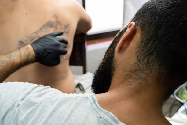 istock Professional master tattoo artist drawing tattoos picture on man's back using machine wearing black gloves at studio salon body art 1160660686
