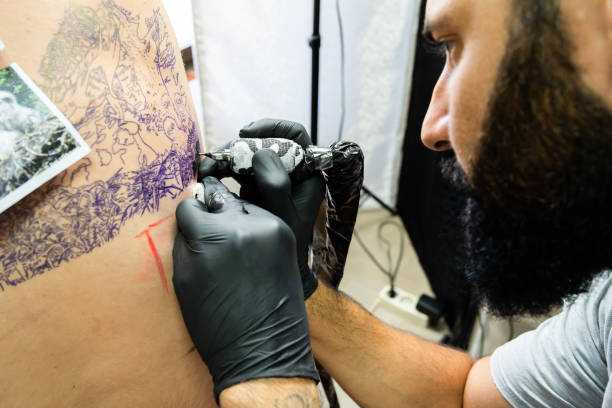 istock Professional master tattoo artist drawing tattoos picture on man's back using machine wearing black gloves at studio salon body art 1160661912