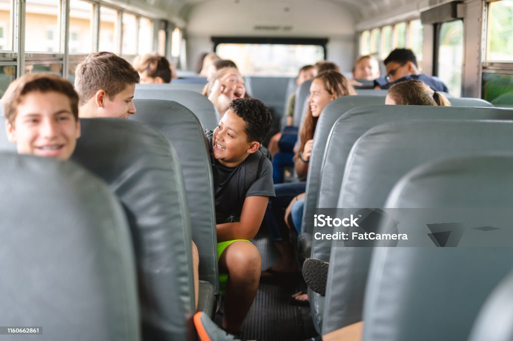 Elementary-age students riding school bus Elementary-age students sit and visit with each other as they ride the bus to school. The focus is on an ethnic pre-teen boy who  talking and laughing with a classmate. School Bus Stock Photo
