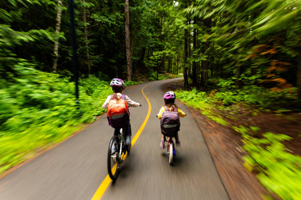Kids biking to school on a pathway through a lush forest. Bike to school for a sustainable lifestyle. Sisters going to school.