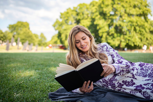 Relaxed mid adult Caucasian woman enjoying a good book in the park during a London summer city break.