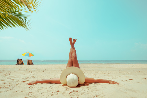 Leisure in summer - Young woman in straw hat lying sunbathe on a tropical beach. Memories of summer vacation concept. retro color tone.