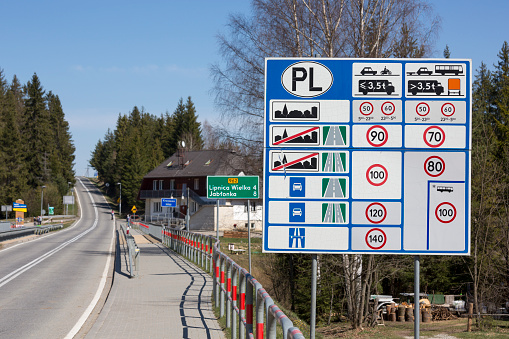 A country road leads from Slovakia into Poland, in Western Europe.  A multi-faceted road warning sign and information sign conveys details about driving requirements in Poland.