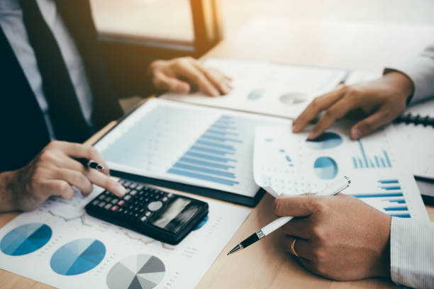 istock Two business people analyzing summary graph reports of business operating expenses and using calculator profit calculation in the office. 1160675036