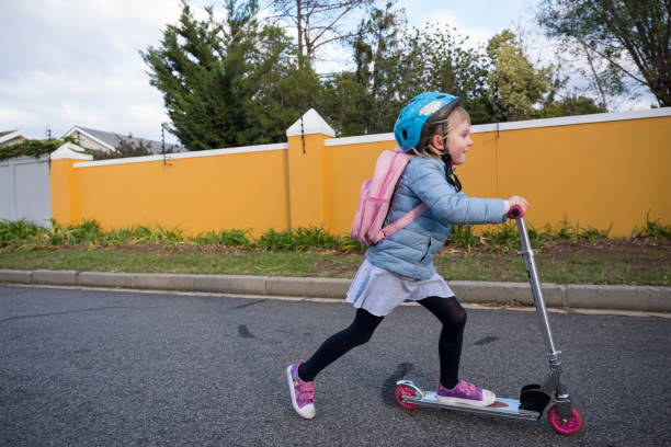 A young girl enjoys riding her push scooter to school. She is riding down a quiet road and wearing a helmet.