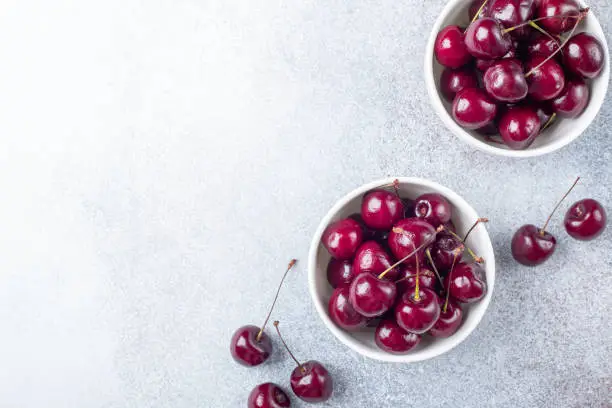 Photo of Fresh ripe red cherries in a white bowl on a gray stone background Copy space