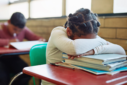Shot of a young girl sleeping at her desk in a classroom