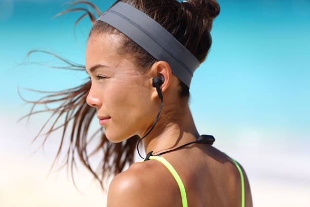 Fitness girl with sport in-ear wireless headphones Fitness girl with sport in-ear wireless headphones. Asian female athlete woman runner wearing Bluetooth earphones with wing tip design for sports activities. Portrait closeup. in ear headphones stock pictures, royalty-free photos & images