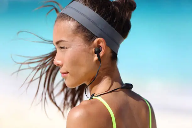 Fitness girl with sport in-ear wireless headphones. Asian female athlete woman runner wearing Bluetooth earphones with wing tip design for sports activities. Portrait closeup.