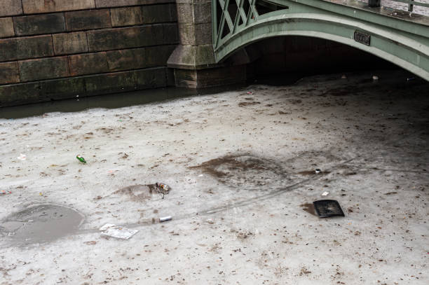 istock Trash, empty bottles and cans on the partly melted ice in a canal. 1160698800