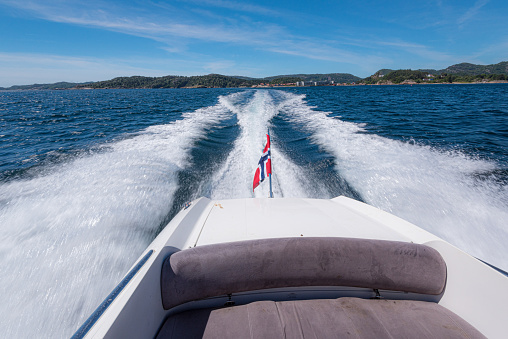 White speed boat racing across a fjord on a sunny summer day.