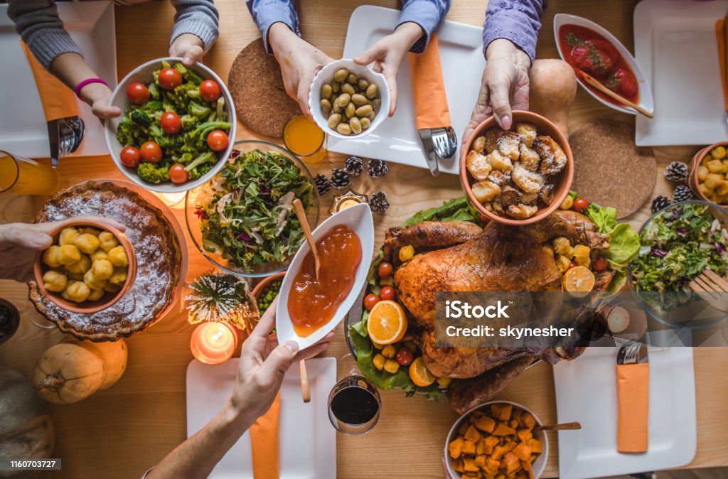 Above view of passing food during Thanksgiving dinner. High angle view of unrecognizable people passing side dishes during Thanksgiving dinner at dining table. Thanksgiving - Holiday Stock Photo