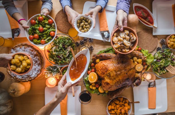 Above view of passing food during Thanksgiving dinner. High angle view of unrecognizable people passing side dishes during Thanksgiving dinner at dining table. side dish stock pictures, royalty-free photos & images