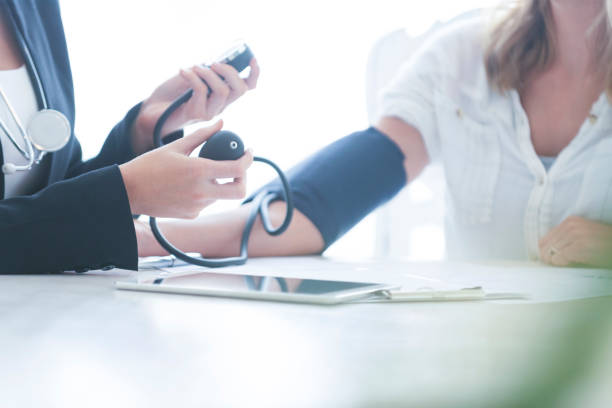Young Woman having her blood pressure taken. Young Woman having her blood pressure taken. She is at home with the doctor using a blood pressure gauge. There is a digital tablet on the table. tablet pc and digital hospital tools stock pictures, royalty-free photos & images