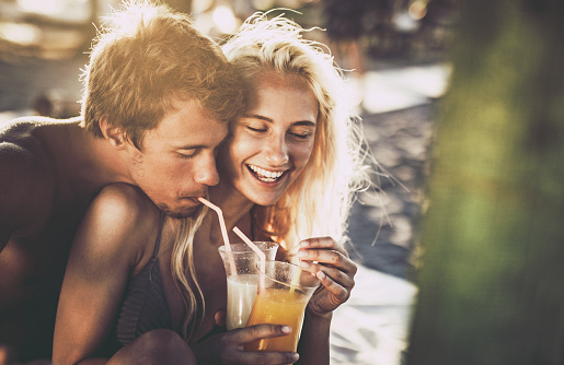 Happy couple in love sharing their drinks during summer day on the beach.