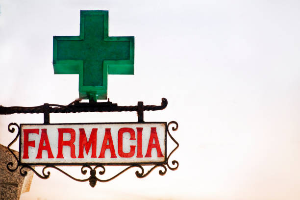 Pharmacy sign in spanish language, cast iron decorative frame, green cross symbol. Dusk background, copy space on the right.