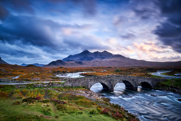 Sligachan old Bridge, Isle Of Skye, Scotland. Sligachan bridge during sunset and a partly cloudy sky, the water flows quickly under the bridge. In the background you can see the mountains on Skye.
