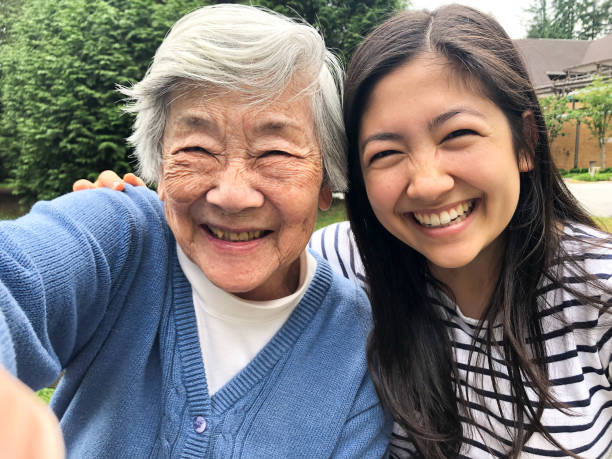 Grandmother in 90s Taking Selfie with Granddaughter Outside Retirement Home Happy Chinese grandma in her 90s taking selfie with granddaughter in her 20s outside in park. taken on mobile device photos stock pictures, royalty-free photos & images