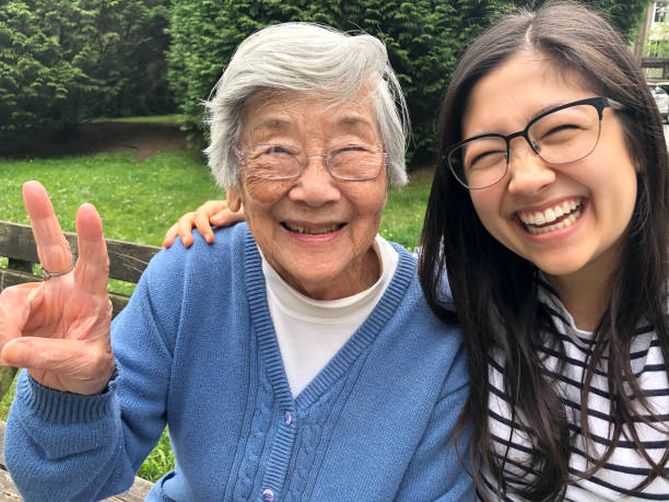 asiatische großmutter und eurasische enkelin lächelnd für foto auf bank - großmutter fotos stock-fotos und bilder