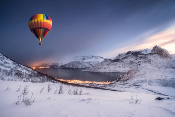 Hot air balloon flying on snow hill with fordgard town in winter Hot air balloon flying on snow hill with fordgard town in winter at Segla island, Norway senja island photos stock pictures, royalty-free photos & images