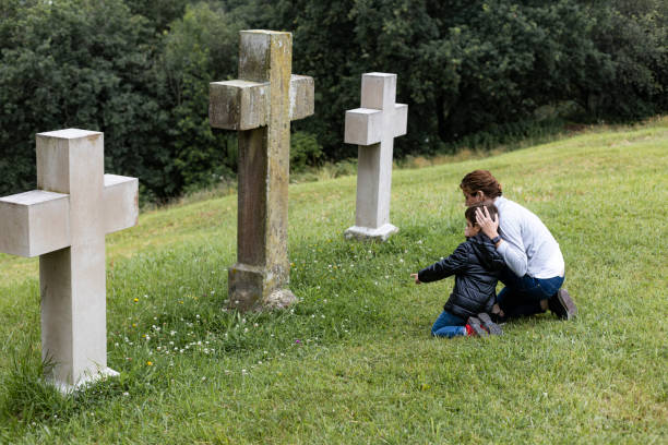 mother and son in front of a cross - cemetery child mourner death imagens e fotografias de stock