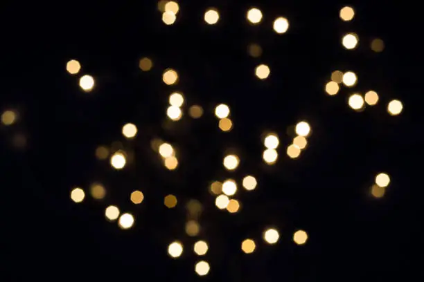 Flying golden bokeh lights in hexagon shape on black. Holiday concept.