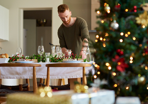 Shot of a young man setting a table for a Christmas party at home