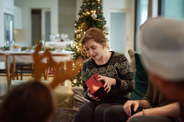 Oooh...what could it be? Shot of young friends opening their Christmas gifts together at home unwrapping stock pictures, royalty-free photos & images