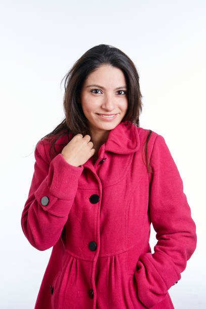A pretty young brunette woman wearing a bright pink coat smiles cheerfully.