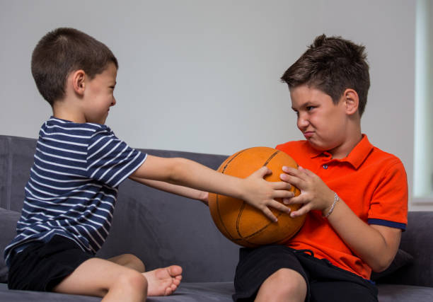 due bambini piccoli, fratelli che litigano per un giocattolo. il conflitto tra bambini su una palla - wrestling sport conflict competition foto e immagini stock