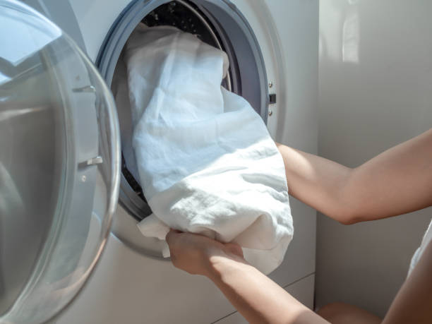 istock Woman's hand putting dirty white linen shirt in washing machine. 1160717708
