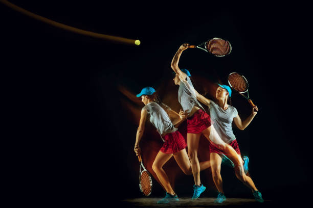 une femme caucasienne jouant au tennis sur le fond noir dans la lumière mélangée - lumière stroboscopique photos et images de collection